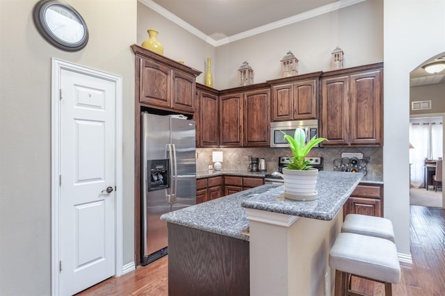 kitchen with decorative backsplash, ornamental molding, light wood-type flooring, and stainless steel appliances