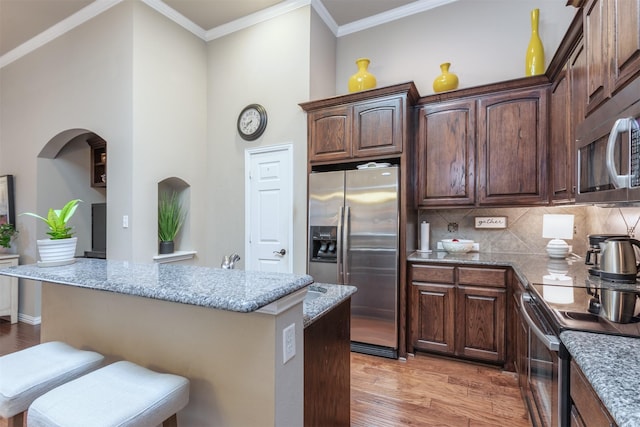 kitchen with light wood-type flooring, a kitchen breakfast bar, backsplash, stainless steel appliances, and light stone countertops