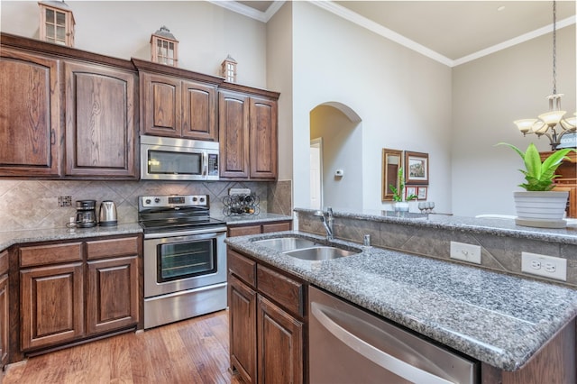 kitchen with light wood-style flooring, ornamental molding, a sink, tasteful backsplash, and stainless steel appliances