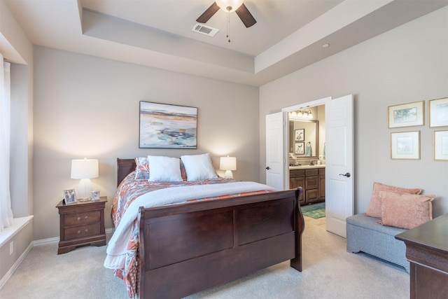 bedroom featuring a tray ceiling, light colored carpet, visible vents, and connected bathroom