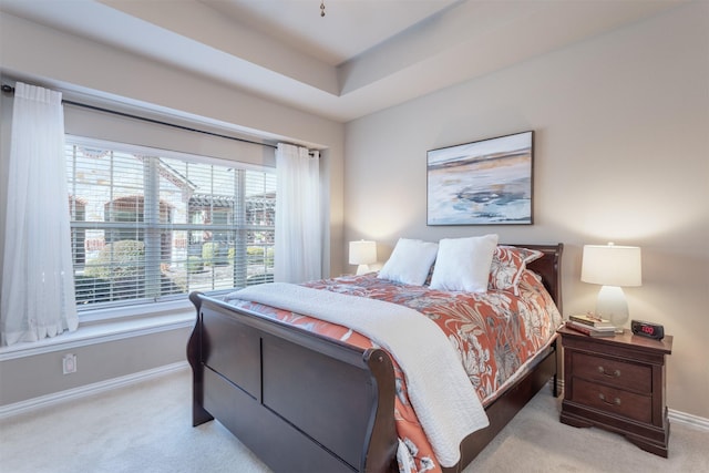 bedroom with a tray ceiling, baseboards, and light carpet