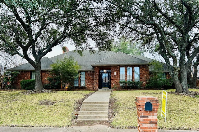 view of front of property with brick siding, a front lawn, and a shingled roof