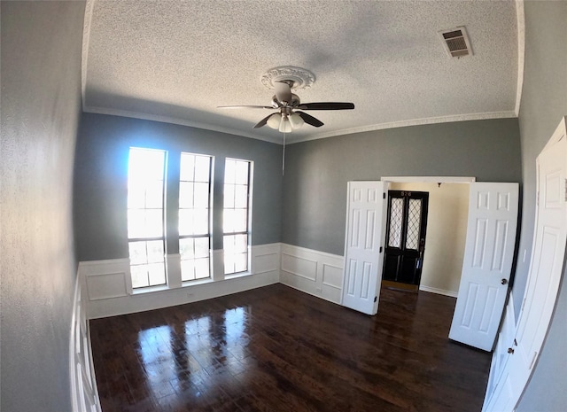 empty room with visible vents, dark wood-type flooring, a ceiling fan, and crown molding