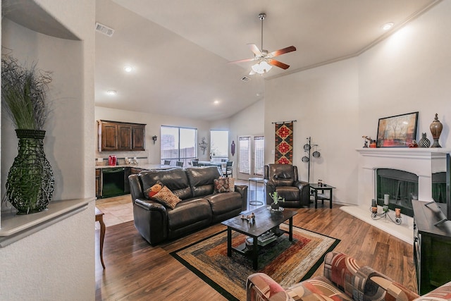 living room with visible vents, a fireplace with raised hearth, ceiling fan, wood finished floors, and high vaulted ceiling