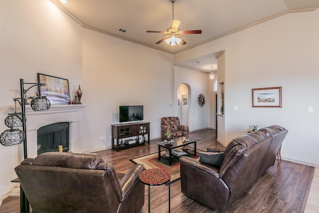 living area with wood finished floors, visible vents, a fireplace, arched walkways, and ornamental molding