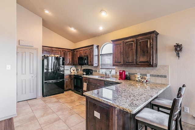 kitchen featuring light stone countertops, dark brown cabinetry, a breakfast bar, a peninsula, and black appliances