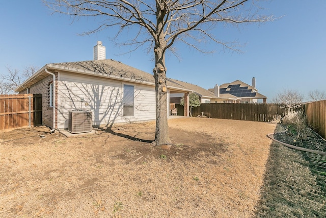 rear view of property featuring cooling unit, brick siding, a fenced backyard, and a chimney