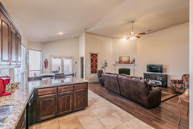 kitchen featuring light wood-type flooring, light stone counters, a peninsula, a fireplace, and dark brown cabinets