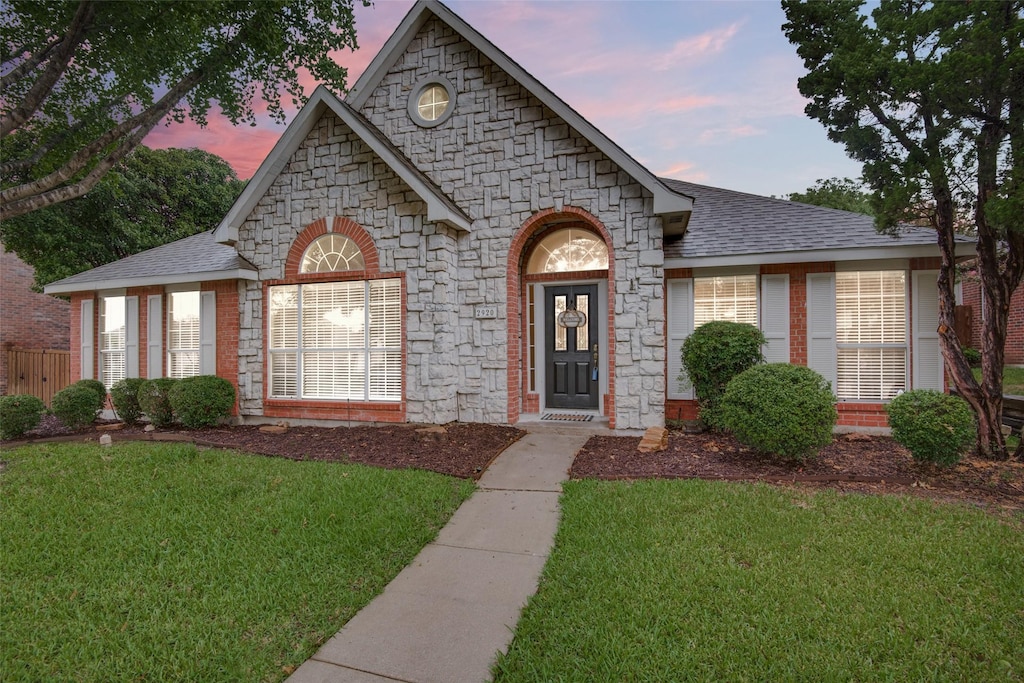 french country home with stone siding, a front lawn, and a shingled roof