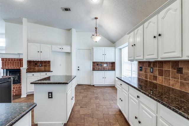 kitchen featuring visible vents, white cabinetry, dark stone counters, a fireplace, and decorative backsplash