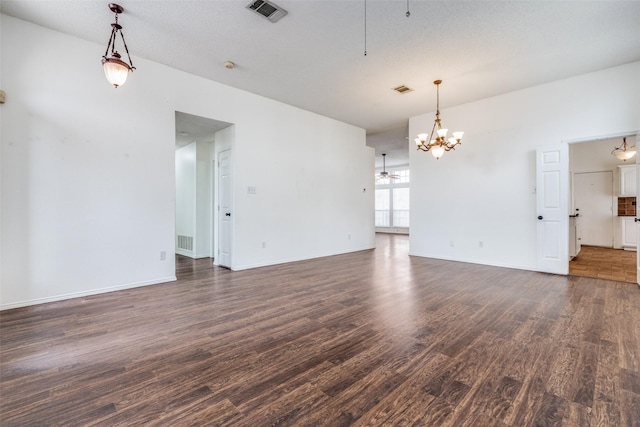 spare room featuring dark wood-style floors, visible vents, ceiling fan with notable chandelier, and baseboards