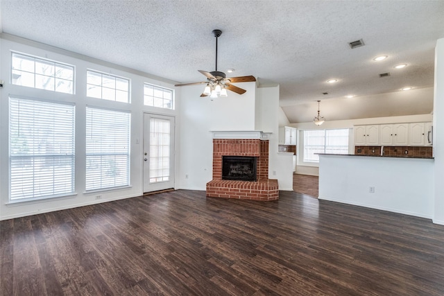 unfurnished living room featuring visible vents, dark wood-style floors, a brick fireplace, ceiling fan, and vaulted ceiling
