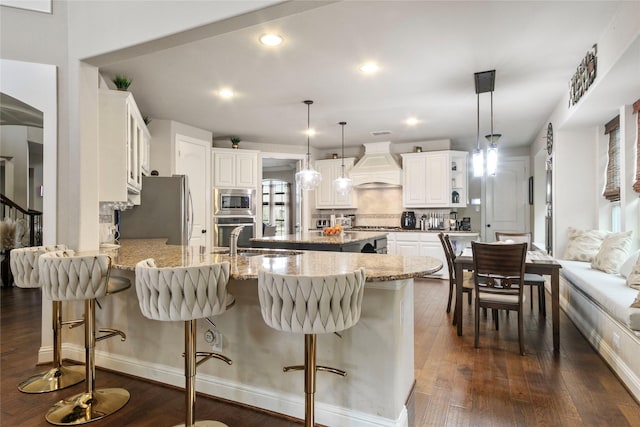 kitchen featuring dark wood-type flooring, custom range hood, a sink, appliances with stainless steel finishes, and a peninsula