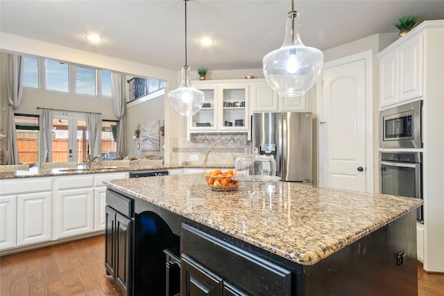 kitchen with wood finished floors, light stone countertops, a kitchen island, a sink, and appliances with stainless steel finishes