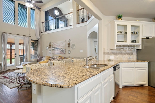 kitchen with a sink, light stone counters, stainless steel appliances, glass insert cabinets, and dark wood-style flooring