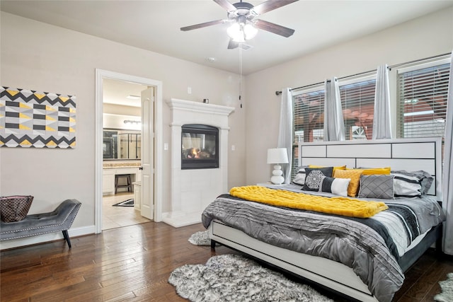 bedroom with connected bathroom, baseboards, a tile fireplace, and hardwood / wood-style flooring