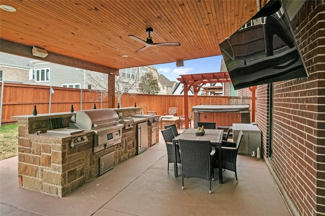 view of patio / terrace with a hot tub, exterior kitchen, a fenced backyard, outdoor dining space, and a grill