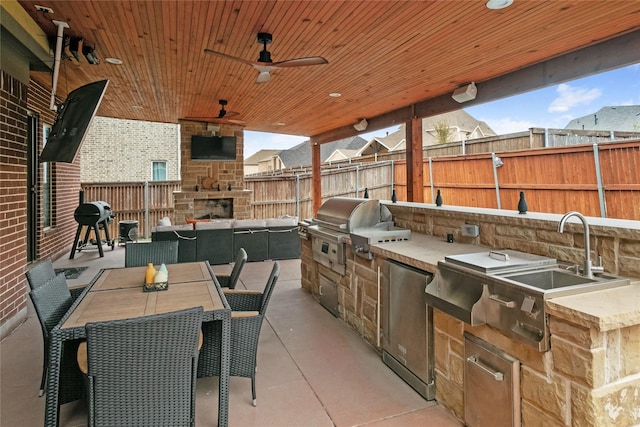 view of patio featuring outdoor dining space, fence, grilling area, an outdoor stone fireplace, and exterior kitchen