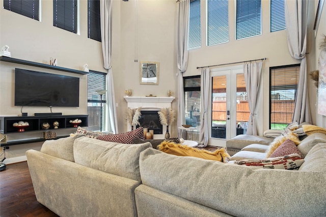 living room with a glass covered fireplace, french doors, dark wood-style floors, and a towering ceiling