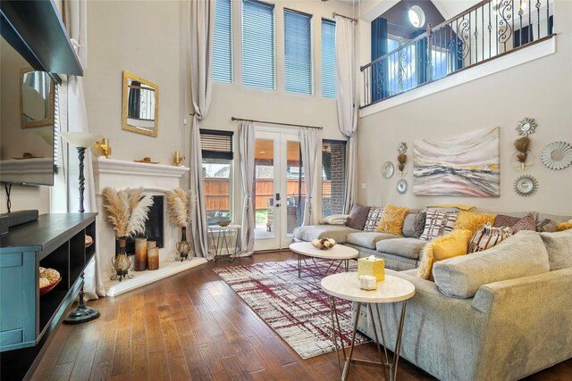 living area featuring french doors, wood-type flooring, a high ceiling, and a fireplace with raised hearth