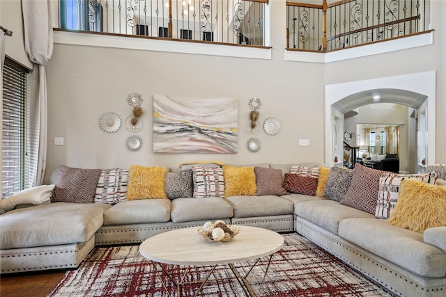 living area with arched walkways, a towering ceiling, and wood finished floors