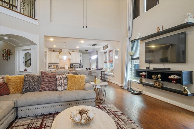 living area featuring baseboards, hardwood / wood-style floors, and a towering ceiling