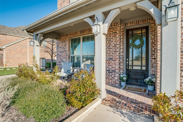 view of exterior entry featuring brick siding and covered porch