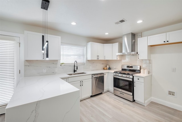 kitchen with visible vents, light wood-type flooring, a sink, appliances with stainless steel finishes, and wall chimney range hood