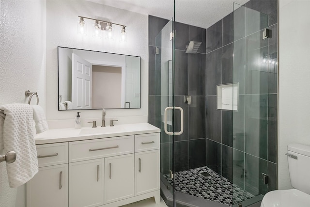 full bath featuring vanity, a stall shower, a textured ceiling, toilet, and a textured wall