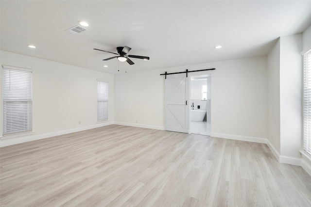 empty room featuring light wood-type flooring, a barn door, visible vents, and recessed lighting