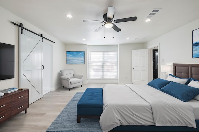 bedroom with visible vents, recessed lighting, light wood-style floors, and a barn door