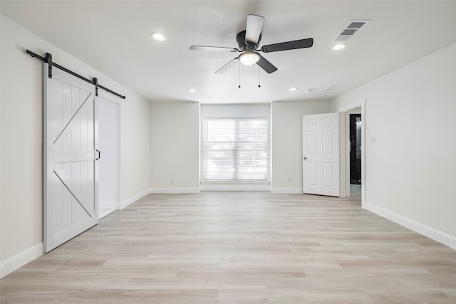 unfurnished bedroom with a barn door, light wood-style floors, visible vents, and baseboards