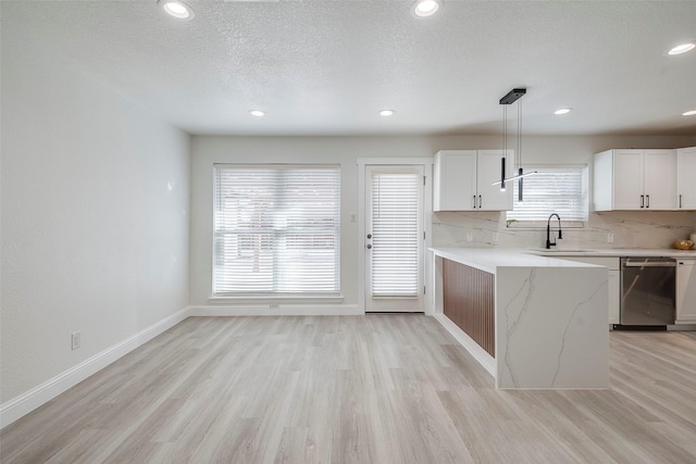 kitchen featuring light wood finished floors, white cabinetry, a sink, stainless steel dishwasher, and backsplash