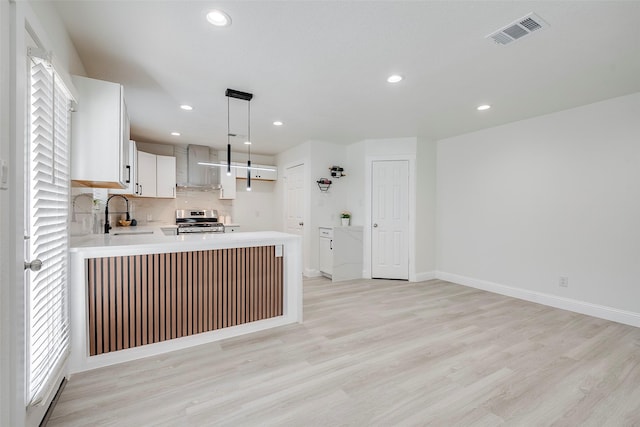 kitchen featuring visible vents, a sink, stainless steel range with gas cooktop, a peninsula, and light countertops