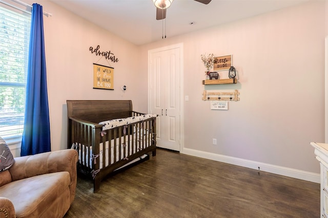 bedroom featuring a crib, a ceiling fan, baseboards, and dark wood-style flooring