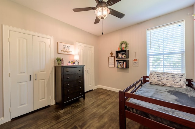 bedroom with dark wood finished floors, baseboards, two closets, and ceiling fan