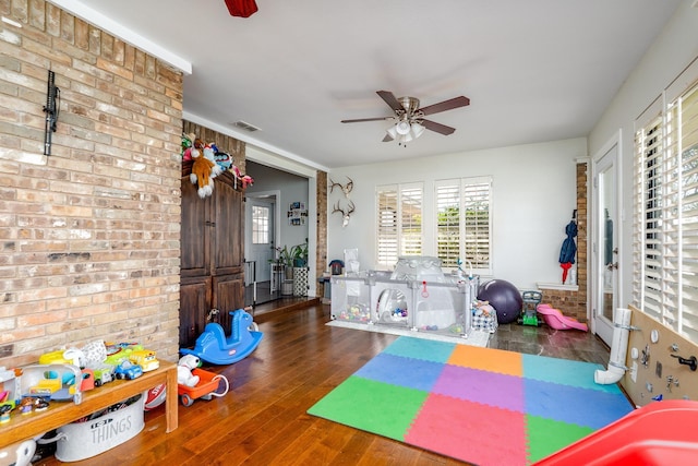 playroom featuring hardwood / wood-style floors, a ceiling fan, visible vents, and brick wall