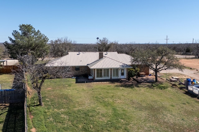 back of house with fence, a standing seam roof, a yard, a chimney, and metal roof