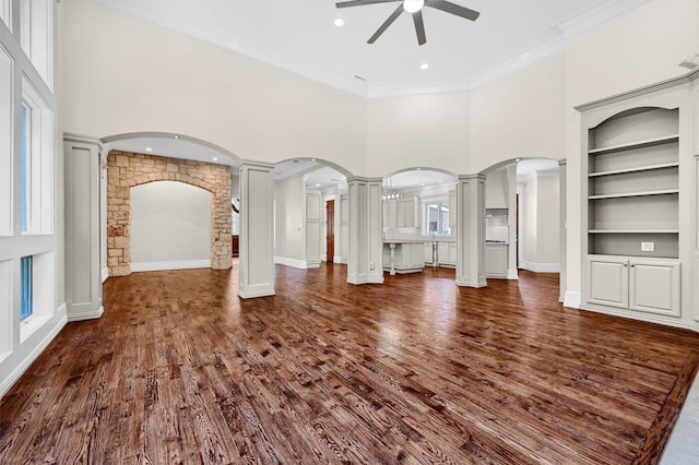 unfurnished living room with built in shelves, dark wood-type flooring, ornamental molding, decorative columns, and ceiling fan