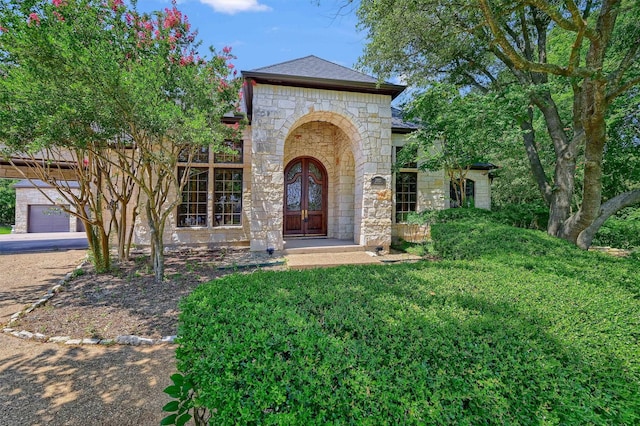 view of front facade with french doors, stone siding, and a shingled roof