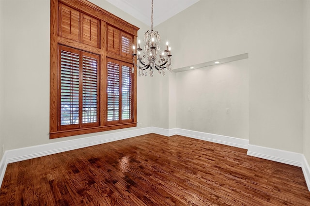 unfurnished room featuring an inviting chandelier, dark wood-type flooring, and baseboards