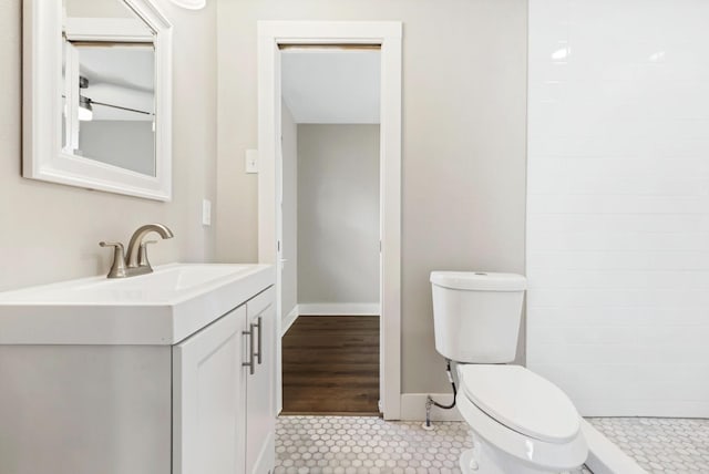 bathroom with toilet, vanity, baseboards, and tiled shower