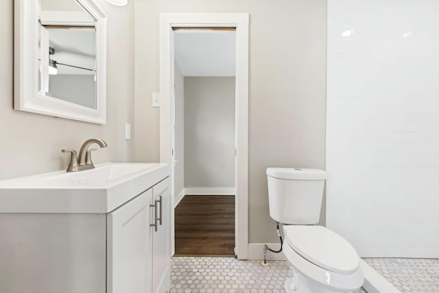 full bath with a tile shower, toilet, vanity, and baseboards