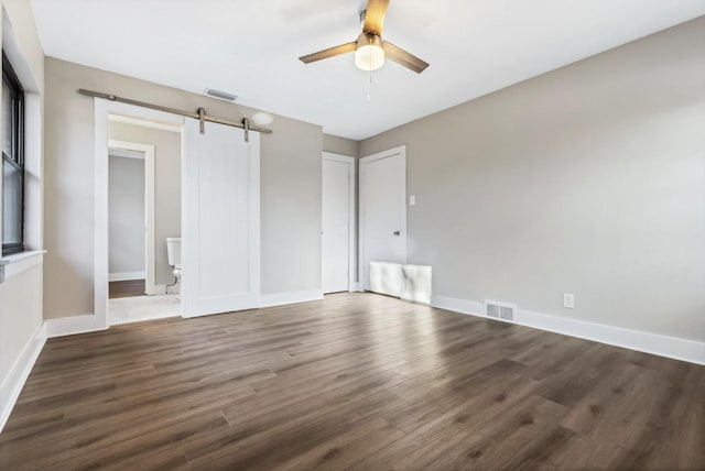 unfurnished room featuring a ceiling fan, a barn door, wood finished floors, baseboards, and visible vents
