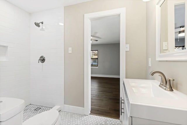 bathroom featuring baseboards, a tile shower, toilet, and a sink