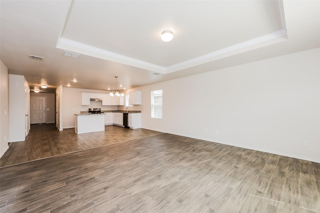 unfurnished living room with a raised ceiling, wood finished floors, and visible vents