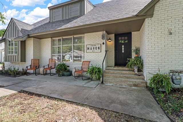 doorway to property featuring brick siding and a shingled roof