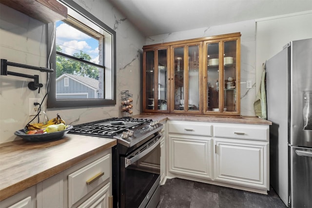 kitchen featuring glass insert cabinets, wood counters, range with gas cooktop, and stainless steel refrigerator with ice dispenser