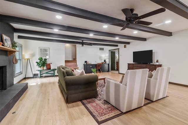 living area featuring light wood finished floors, visible vents, a fireplace with raised hearth, baseboards, and beamed ceiling