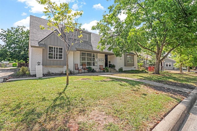 view of front of house featuring fence, board and batten siding, a front yard, a shingled roof, and brick siding